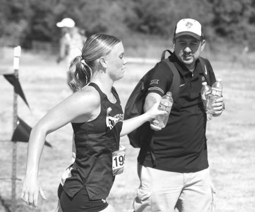 WATER IS BETTER – Kenny “Bobby Boucher” Lunsford hands off a bottle of water to Scout Snodgrass as she’s running the pre-state meet. Runners competed in temperatures in the mid- to upper-90s during the meet. [KT&FP Staff Photo]
