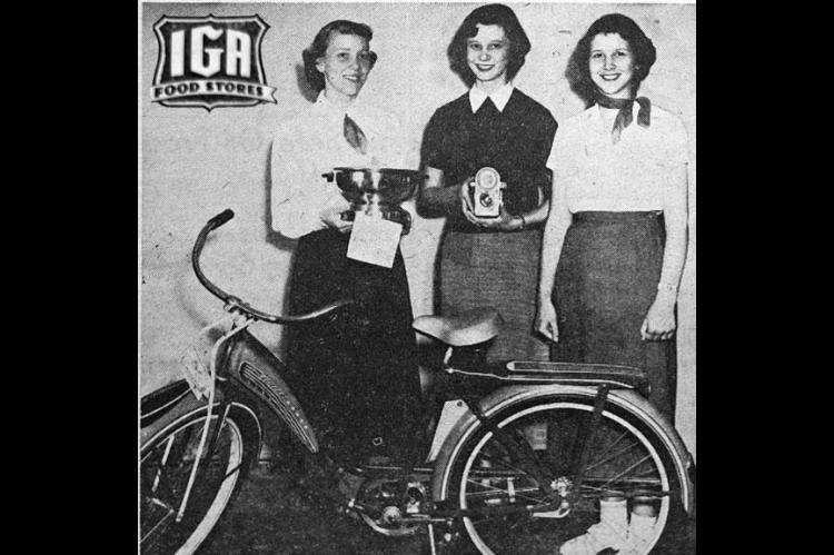 The three girls above are holding the prizes they won in our “Miss IGA Teenager” contest. Dennis Wood, left, won an electric popcorn popper for third prize. Evelyn Phillips, center, won a camera and flashbulbs for second prize. The champion and winner of the “Miss Teenager” title was Greta Boyd, right, who received the bicycle. (Times, April 26, 1951)