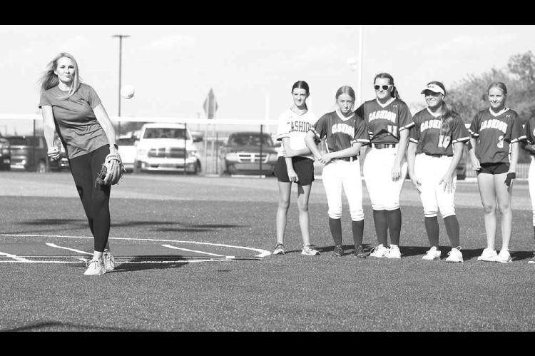 STILL GOT IT – Linzee (Roby) Beaman delivers the first pitch as members of the Cashion softball team look on Monday. Cashion was opening its newly-renovated softball complex, which included new turf. Beaman was on Cashion’s first-ever fastpitch team a