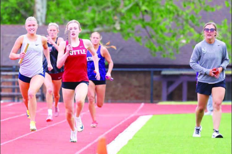 SCOUT SNODGRASS (far left) ran down a pair of runners on her anchor leg of the 1,600 meter relay on Tuesday but ran out of real estate before the finish line and KHS took second in the race. She’s urged on by one of Kingfisher’s track coaches, Nicole Kippenberger (far right). [KT&amp;FP Staff Photo]