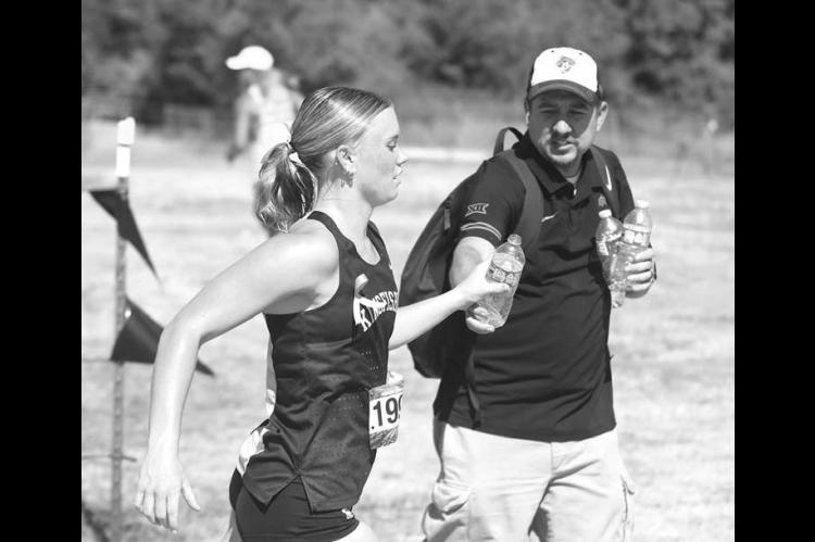 WATER IS BETTER – Kenny “Bobby Boucher” Lunsford hands off a bottle of water to Scout Snodgrass as she’s running the pre-state meet. Runners competed in temperatures in the mid- to upper-90s during the meet. [KT&FP Staff Photo]
