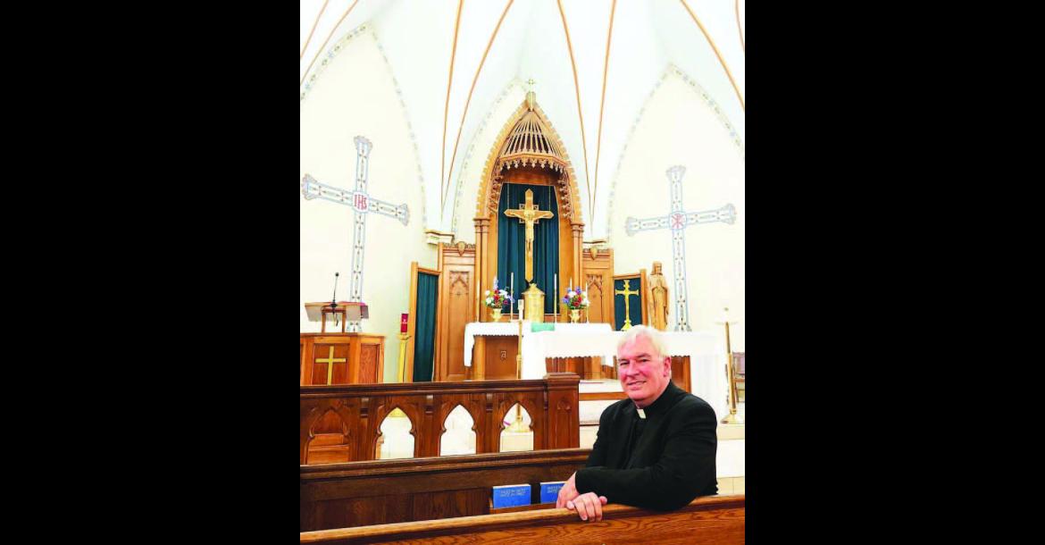 BACK HOME – Reverend Robert Wood sits on a pew inside Sts. Peter &amp; Paul Catholic Church where he spent much of his childhood. Wood returned to serve as the church’s priest in June. [KT&amp;FP Photo by Twila Adams]